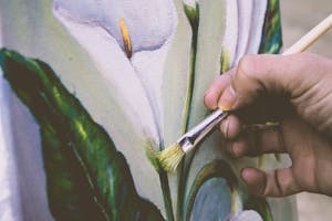 Close-up view of an artist painting a floral design on canvas using a brush.